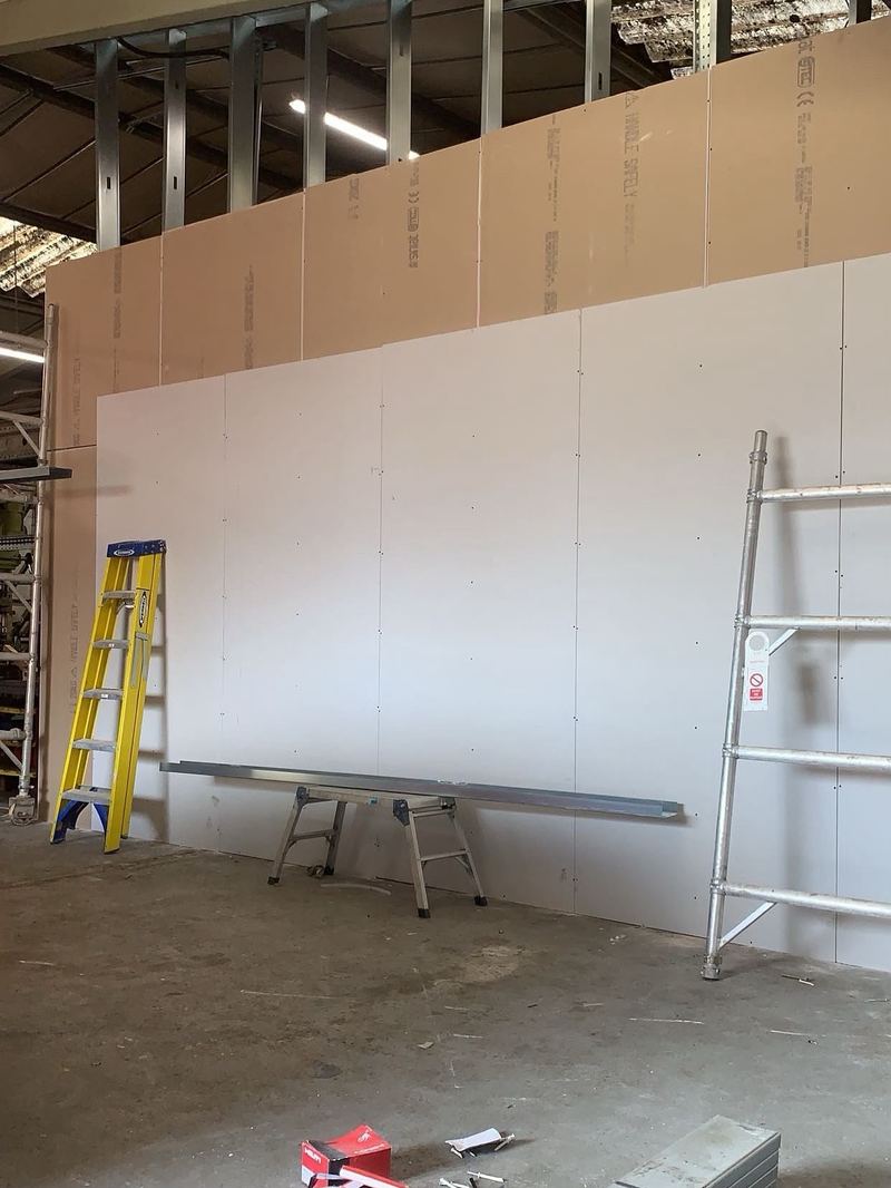 A tall plasterboard wall being drylined inside a commercial unit